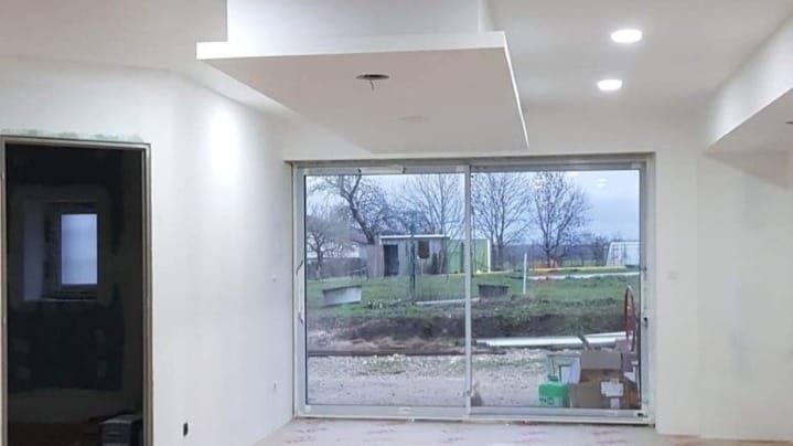 Une pièce en construction avec un plafond moderne, des murs blancs et une grande fenêtre donnant sur un jardin